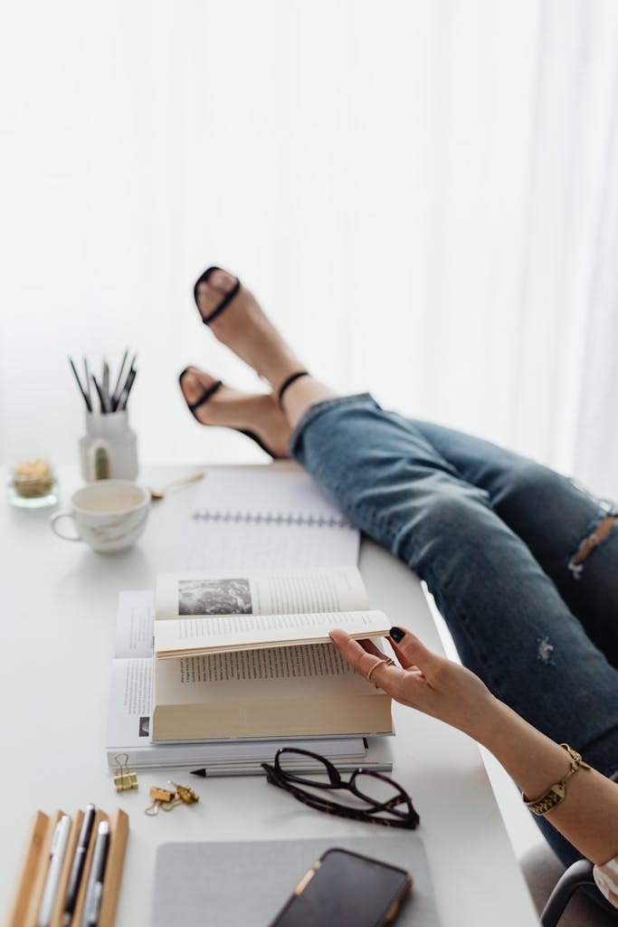 Casual modern desk setup featuring books, coffee, and a relaxed posture with feet up.